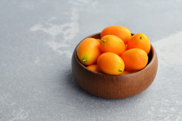 Raw organic kumquat citrus fruits in wooden bowl on concrete background. Healthy vegetarian food. Copy space.