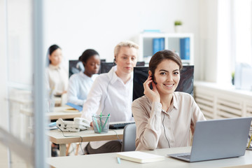 Portrait of female helpdesk operators sitting at in row , focus on smiling woman looking at camera...