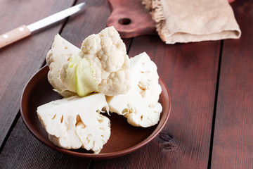 Cauliflower in a ceramic bowl. Sliced fresh cauliflower on wooden boards. Organic cabbage in a clay bowl in rustic style