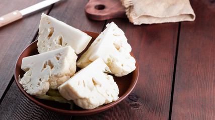 Cauliflower in a ceramic bowl. Sliced fresh cauliflower on wooden boards. Organic cabbage in a clay bowl in rustic style