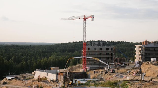 aerial panoramic time lapse of construction site of suburban houses with white red tower crane, truck crane, concrete mixer, concrete feed truck and tractor in the green valley and trees