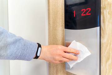 A person presses the Elevator button with toilet paper during an epidemic of coronavirus and infectious diseases. Preventive measures to reduce the spread of the flu virus. Closeup and soft focus.