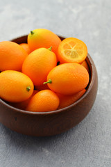 Fresh organic kumquat fruits in wooden bowl on concrete background. Healthy vegan food. Kumquat fruit cut in half.