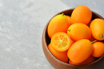 Kumquat fruits in wooden bowl on light stony background. Healthy vegetarian food. Kumquat fruit cut in half. Copy space.