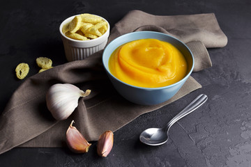 Pumpkin soup in a bowl with spoon with fresh garlic and wheat croutons on dark grunge background. Traditional thanksgiving day meal