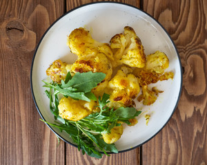 Vegetarian lunch with cauliflower and fresh arugula on a round ceramic plate, close-up