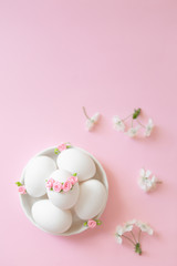 White eggs in bowl on pink background with flowers