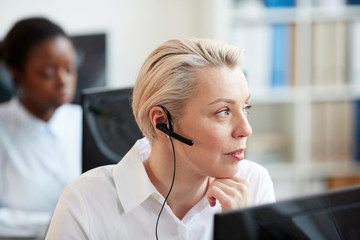 Close up portrait of blonde woman wearing headset and talking to customer while working in support...