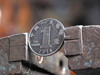 Yuan coin clamped in a metal vise. Currency under the onslaught, the concept of financial problems and crisis