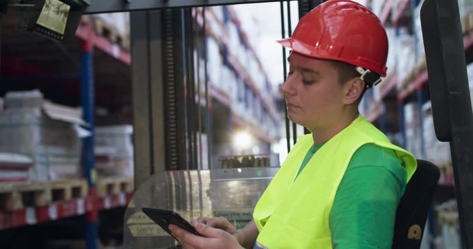 Engineer in uniform controls the telescopic forklift in storage using the tablet