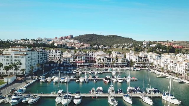 Beautiful Aerial panoramic view of "Puerto de la Duquesa" in MANILVA- Malaga SPAIN. Yachts and boats docked in the Harbour. Luxury Apartment Urbanisation and Restaurants. Drone Truck Left