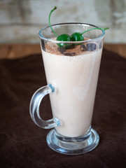 Milk jelly with cocoa and cherry in a tall glass is on the table on a brown napkin