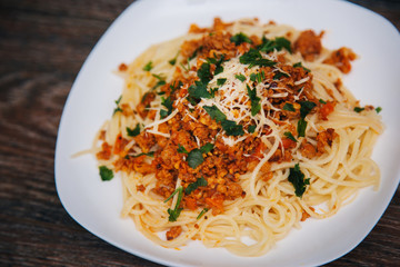 Spaghetti with minced meat in tomato with herbs and cheese on a white plate. Plate with food on a dark wooden table. Lunch with meat.