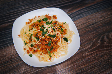Spaghetti with minced meat in tomato with herbs and cheese on a white plate. Plate with food on a dark wooden table. Lunch with meat.
