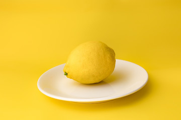 .Template with yellow background. Isolated lemon fruit on white plate. Flatly, top view. Minimal flatly. Healthy food.  Single whole.  Fresh fruit.