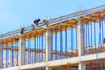 Three workers install a metal frame for a reinforced concrete beam