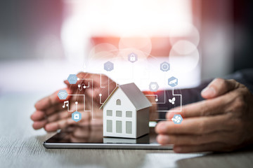 Small house model is on tablet with man's hand and icons home electronics devices connecting with wireless.