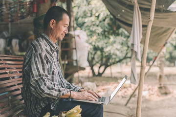 Asian farmer working through laptop and with an blank screen on the farm