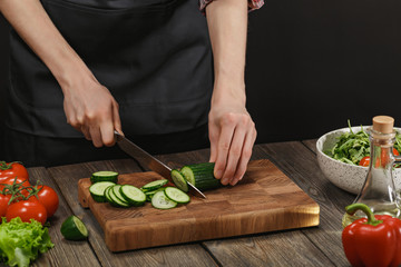 Woman cooking fresh healthy salad. Female hands cutting vegetables on board on wooden table with copyspace.