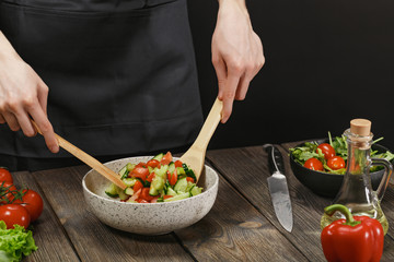 Woman mixing fresh healthy vegetable salad on wooden table. Female hands with copyspace.