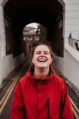 Young girl laughing without makeup and light brown hair with red raincoat. Vertical photo with a tunnel in the background.