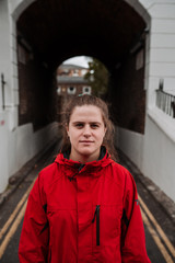 Young girl without makeup and light brown hair with red raincoat and serious face. Vertical photo with a tunnel in the background.