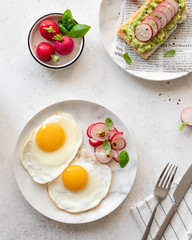 top view of a healthy easy breakfast of fried eggs and toast with mashed avocado, radish and sesame seeds. light concrete background. vertical image