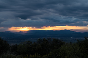 Lumière orangée du coucher de soleil traversant un ciel très nuageux et menaçant au dessus des montagnes des Cévennes (Occitanie, France)