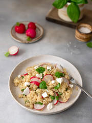 Quinoa salad with feta cheese, radish slices and basil in a ceramic plate. clean eating and vegetarian concept. gray concrete background. vertical image.