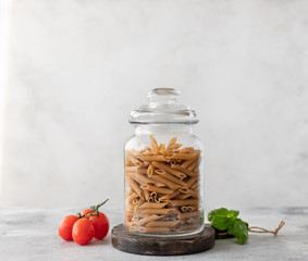Wholewheat penne pasta in a glass container. close-up. diet concept. place for text. Gray...