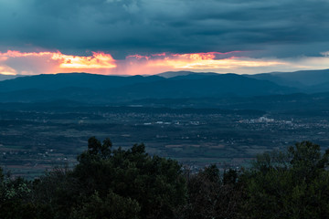 Lumière orangée du coucher de soleil traversant un ciel très nuageux et menaçant au dessus des montagnes des Cévennes (Occitanie, France)
