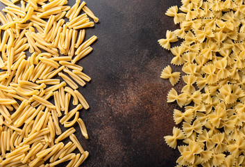 treccia pasta and farfalle pasta on a dark textural background. dry pasta background. top view. place for text.