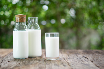Bottles of milk and glass of milk on a wooden table. Blur background of nature.