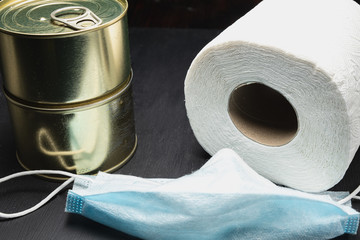 roll toilet paper and two cans of canned food, and medical mask coronavirus virus protection. horizontal. dark background