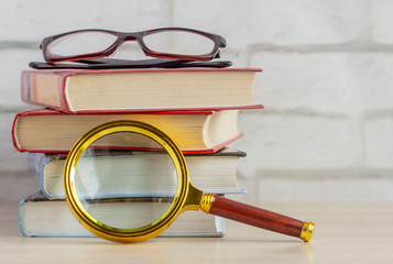 A stack of books, glasses, and a magnifying glass on the table.The concept of information search. - Powered by Adobe