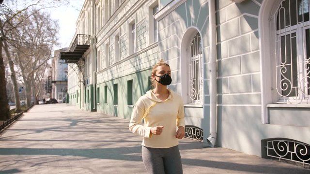 Portrait of beautiful young and fit woman running and jogging alone on the empty street in city center wearing protective face mask, slow motion