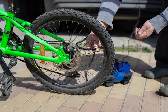 man pumps up a wheel with a compressor on a children's bike. Bicycle service. close-up - Powered by Adobe