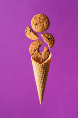 Whole oatmeal cookies and pieces float in the air and fall into a waffle cone on a purple background. Concept of the morning Breakfast.