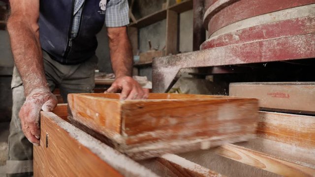 Old farm man sifting cornflour made inside na old windmill to sell