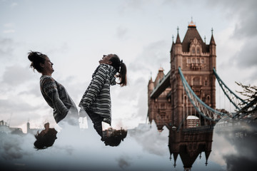Two girls laughing  in front of Tower Bridge, London. Cloudy day with a reflection of the lower half of the photo.