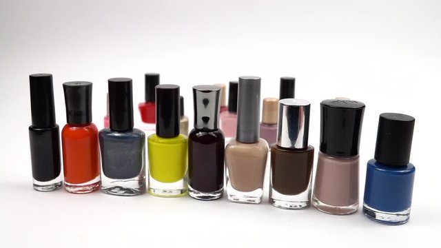 Glass bottles with nail polish of different colors slowly move on a white background, slow motion