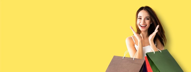 Shopping woman. Very happy excited girl, holding bags, isolated over yellow color background. Copy...
