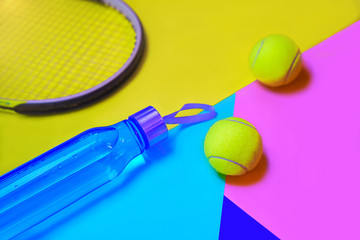 Tennis play layout with tennis balls, racket, bottle of water on abstract different multicolored neon background with place for text.
