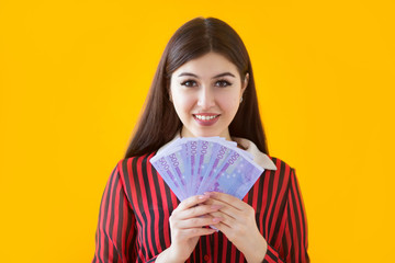 beautiful young woman with euro in hands on a yellow background