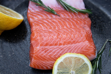 Salmon. Rosemary. Fresh raw salmon filet with cooking ingredients, herbs and lemon on a black background, top view