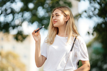 Happy blonde european girl smoke elektronic cigarette on the street