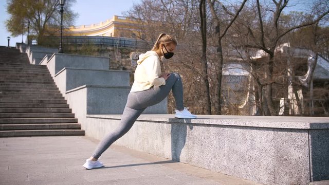 Beautiful young and fit woman doing sport excercises alone on the stairs of city center area wearing protective face mask, slow motion