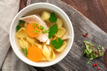 Chicken broth with pasta, carrots, parsley and meat pieces on a wooden background. Homemade soup rustic style