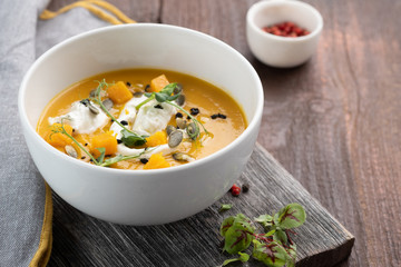 Pumpkin cream soup with seeds and herbs in a white bowl on a wooden background, rustic style