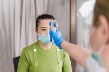 Asian doctor woman wear mask using infrared forehead thermometer gun